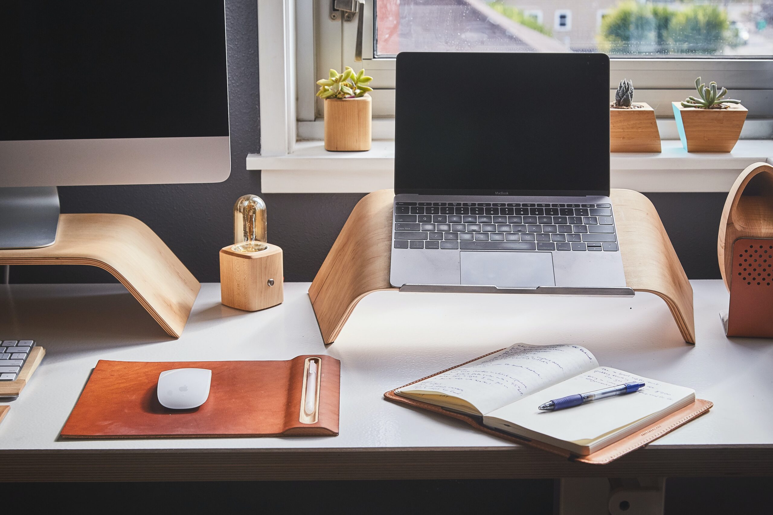 Laptop on wood riser on top of desk showing retreat pricing calculations in notebook.