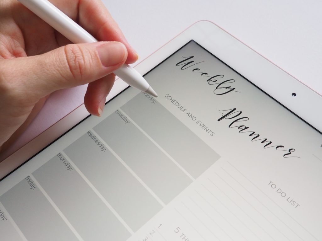 Woman's hand writing out weekly schedule on paper.