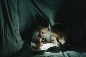 girl and boy reading book in blanket fort