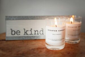 two lighted scented candles with wooden Be Kind sign in background at in-person event