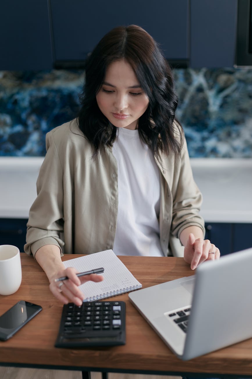 woman using a calculator while sitting in front of a laptop